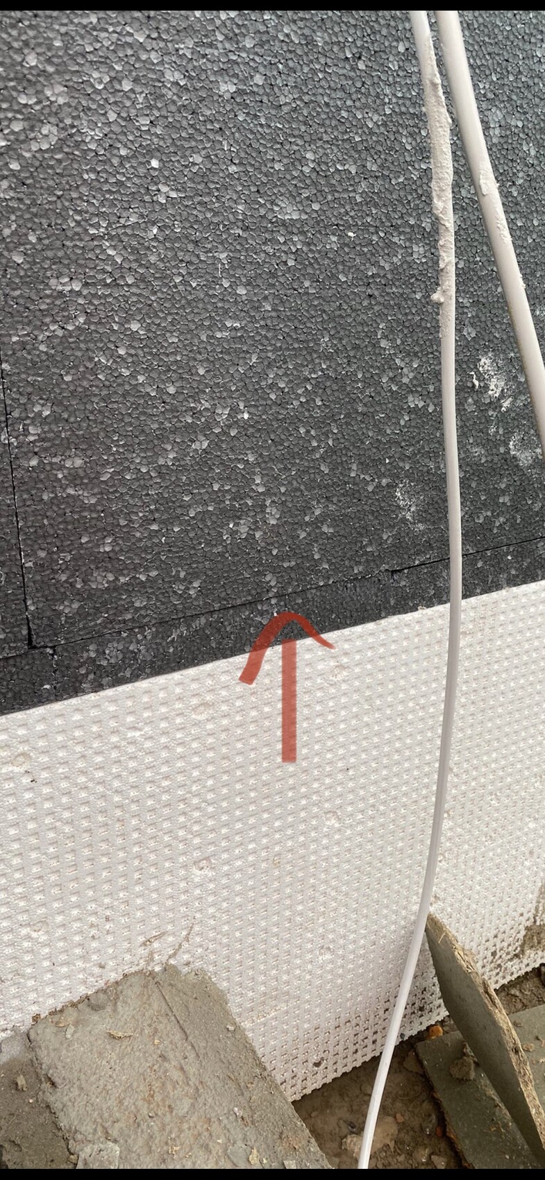 Außenwand mit schwarzer, rauer Dämmoberfläche; unten weiße Dämmplatten; roter Pfeil markiert Fuge.