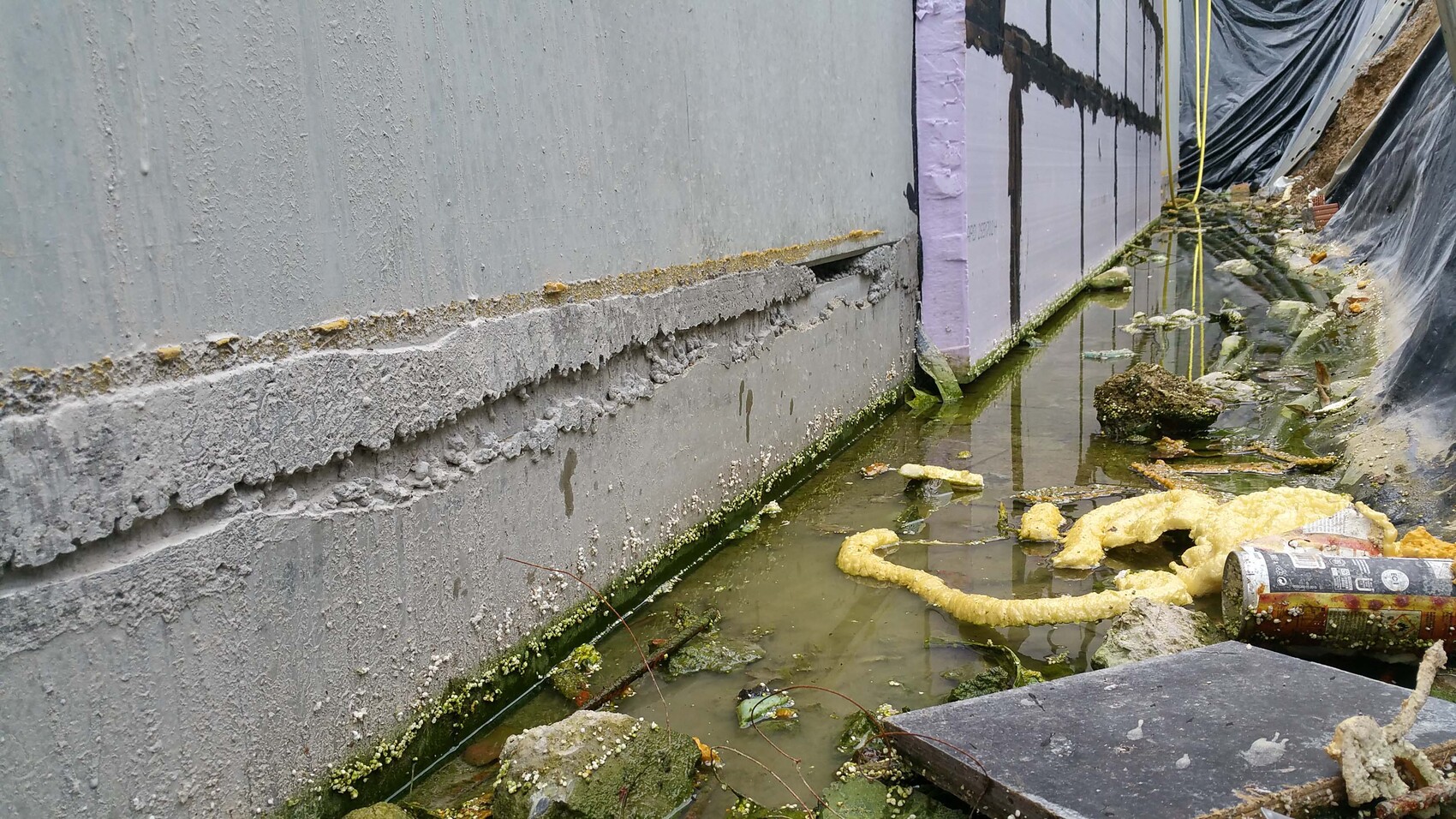 Aussenwand Daemmung am Fundament mit Wasserlache und Baufolie bei Bauarbeiten