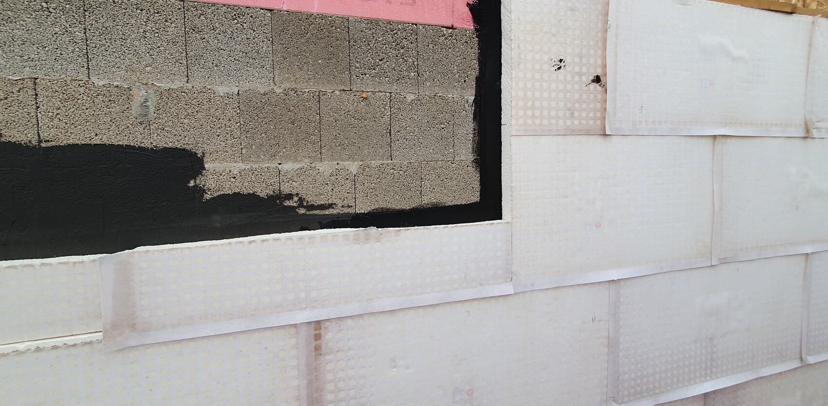 Außenwand im Bau mit Dämmplatten und dunkler Abdichtung