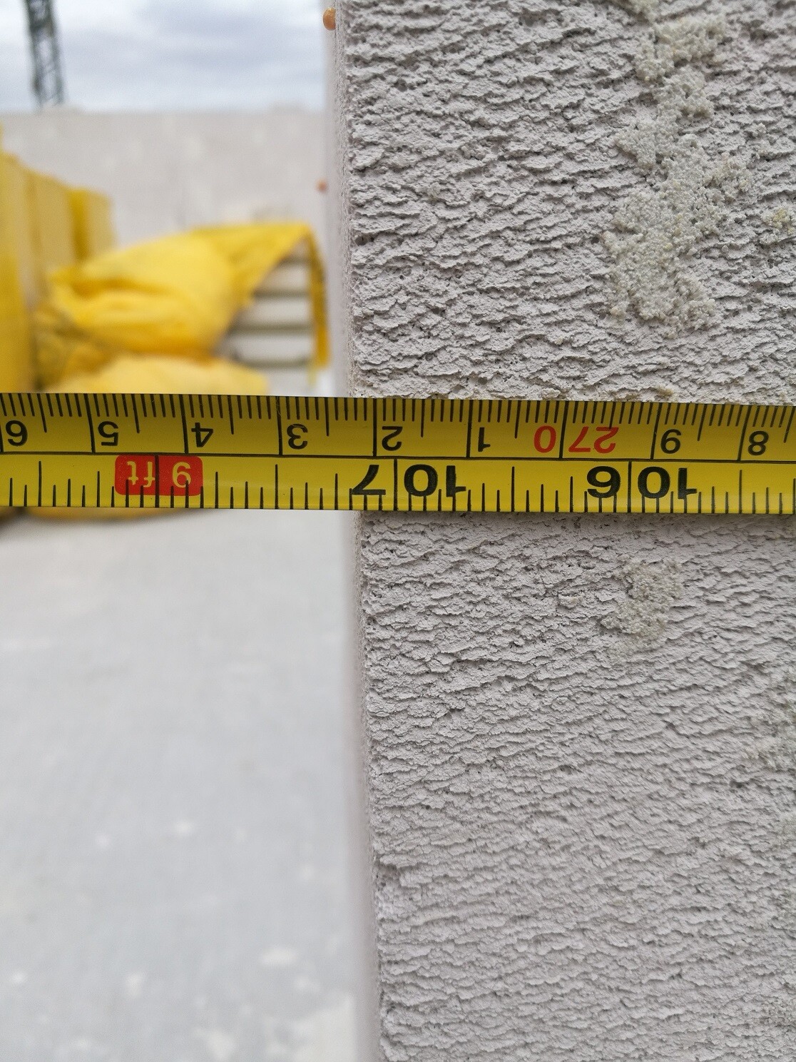 Nahaufnahme einer rauen Außenwand mit Messband im Baustellenhintergrund.
