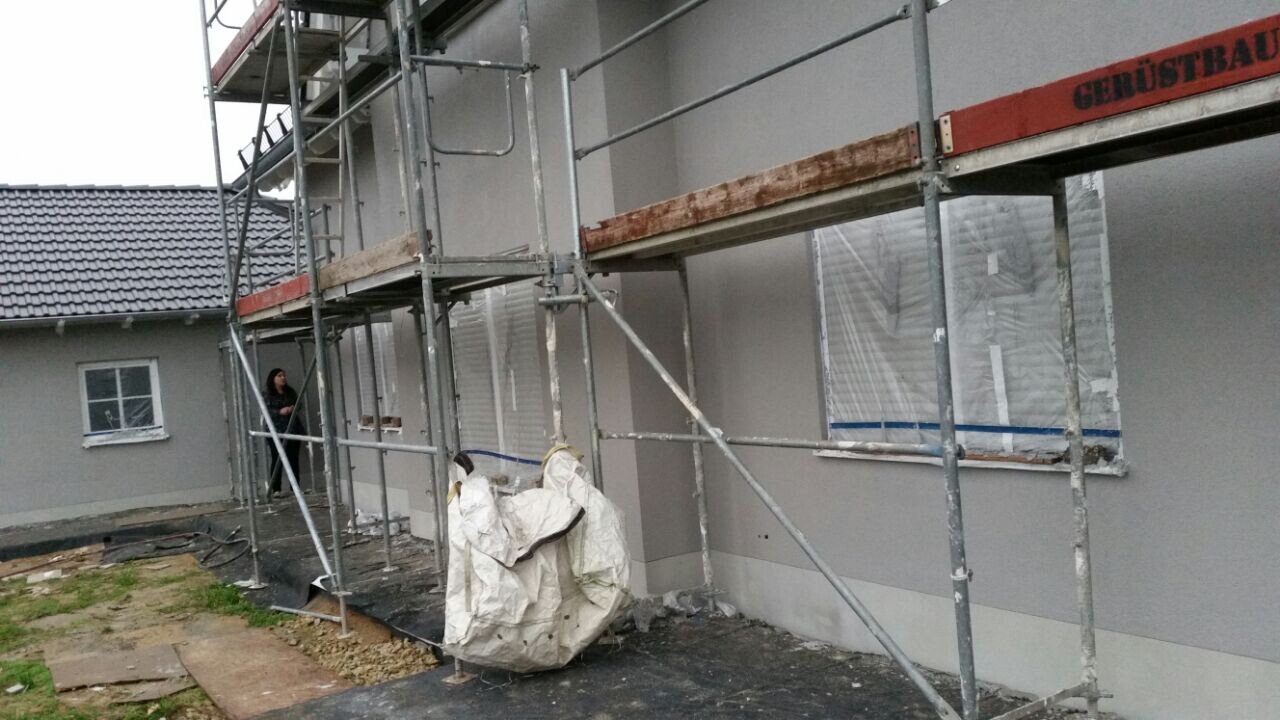Baustelle am Wohnhaus; Gerüste, eine Person steht am Eingang, weißer Abfallbeutel auf dem Boden.