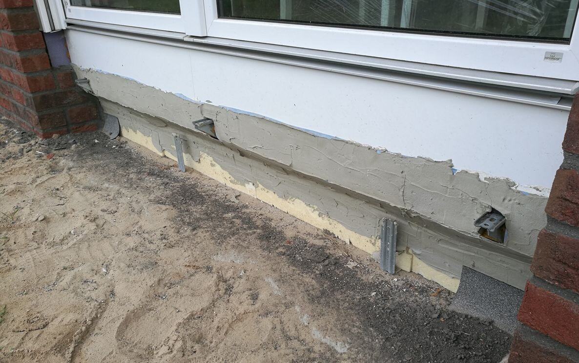 Außenwand am unteren Putzbereich mit Rissen und sichtbarer Dämmung am Fundament
