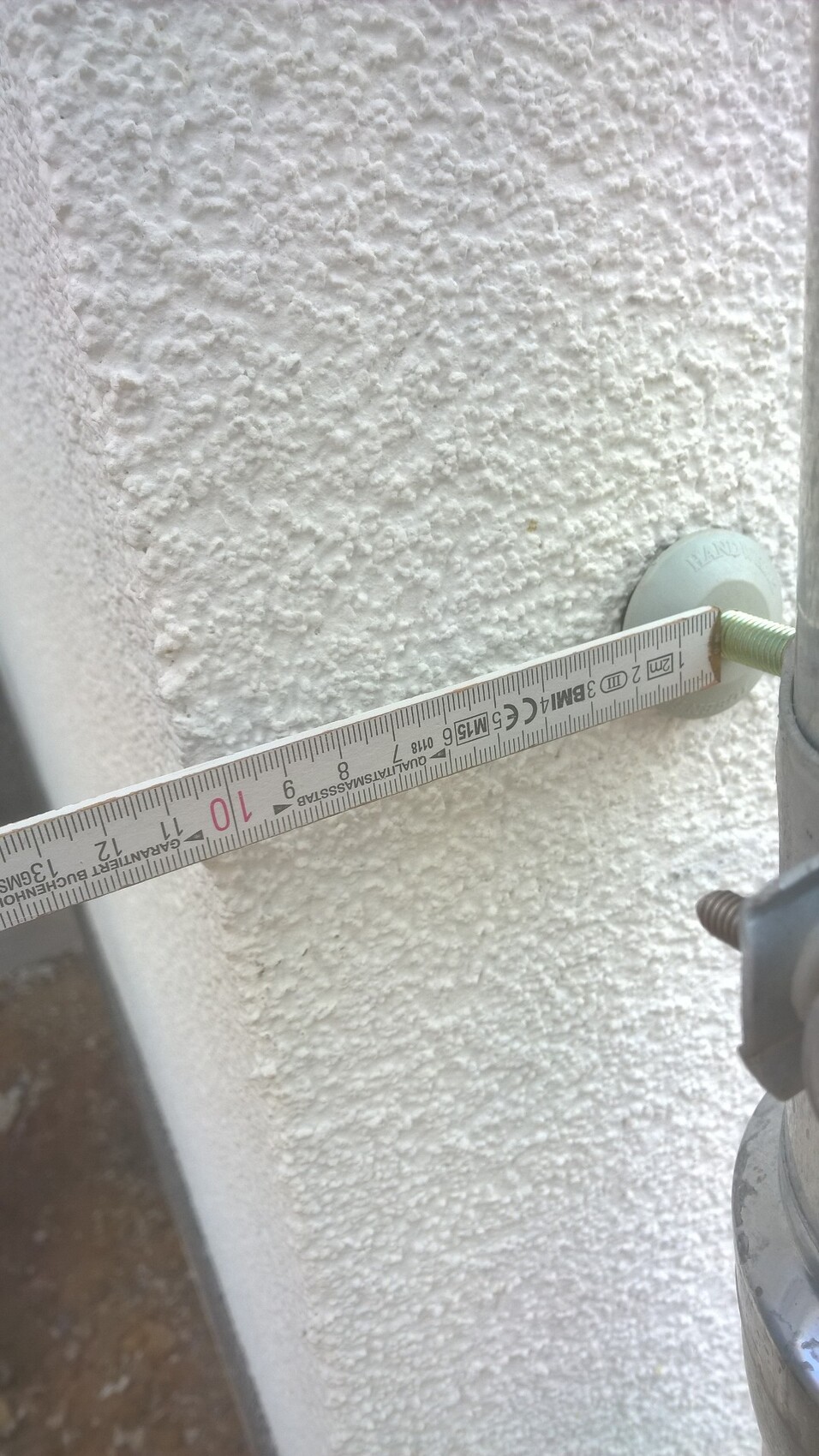 Außenwand mit grobem Putz und Messband zur Vermessung der Struktur