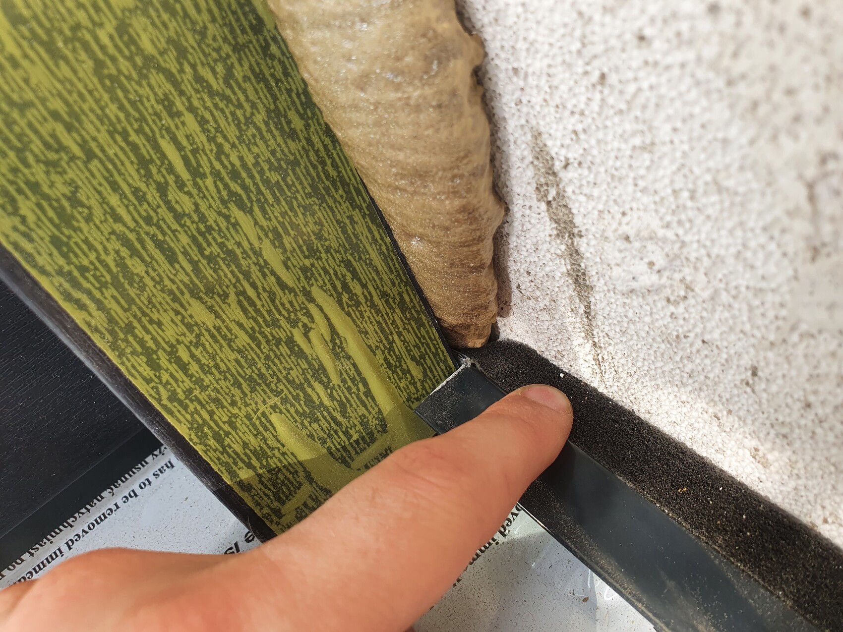 Hand drückt schwarzen Dichtungsstreifen in Fuge zwischen grünem Holzpaneel und rauer Wand.