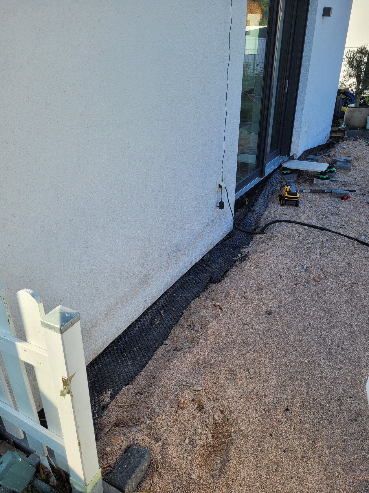 Außenwand eines Hauses; Boden mit schwarzer Drainagematte, Werkzeugen und Kabel.
