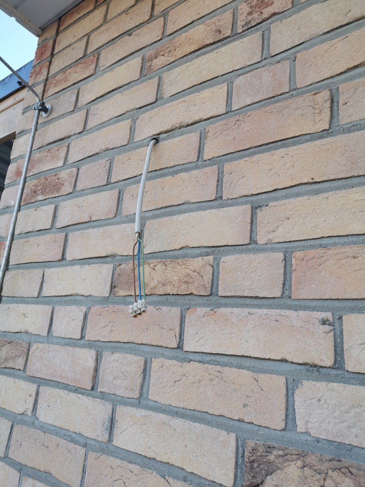 Außenwand aus Ziegeln; weißes Kabelrohr hängt senkrecht und endet in Steckverbinder.