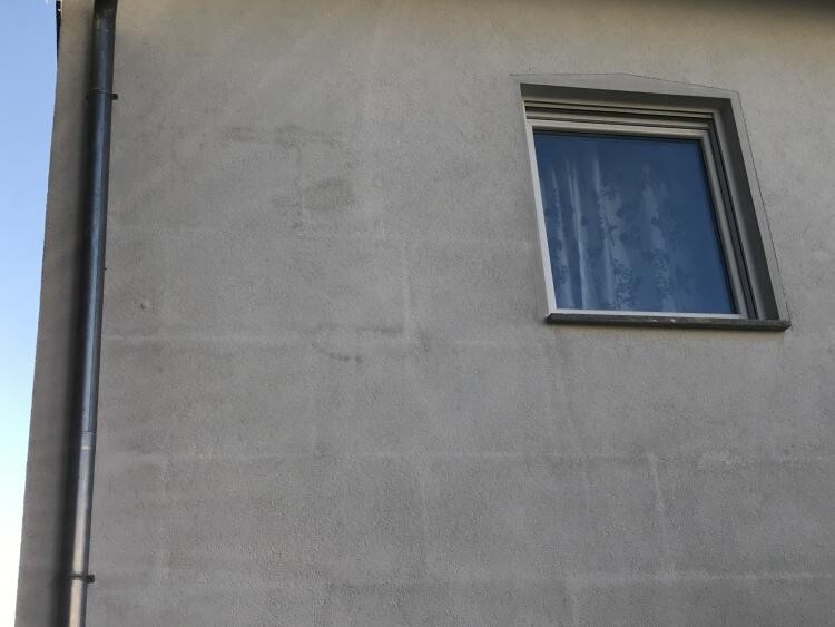 Außenwand eines Hauses mit kleinem rechteckigem Fenster und Regenrinne links.