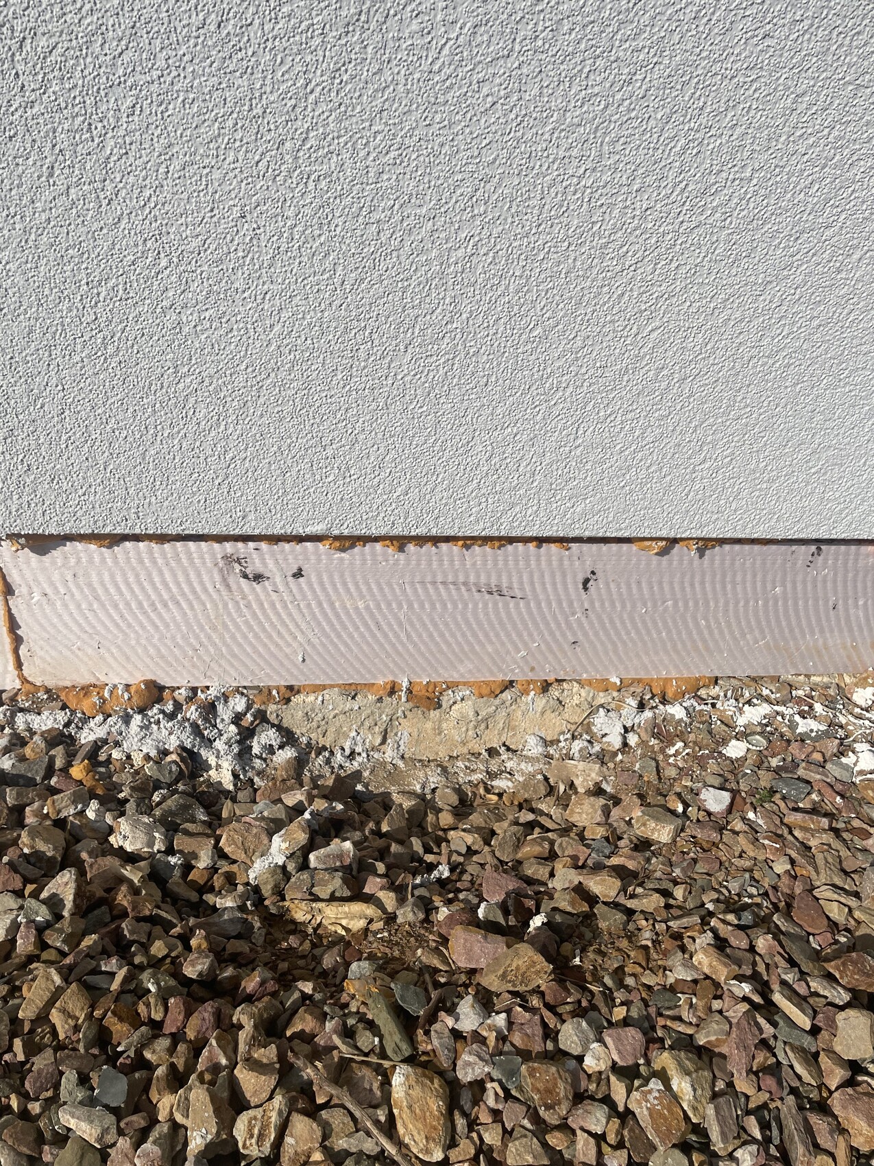 Außenwand mit grauem Putz, darunter rosa Dämmschicht und Kiesboden.