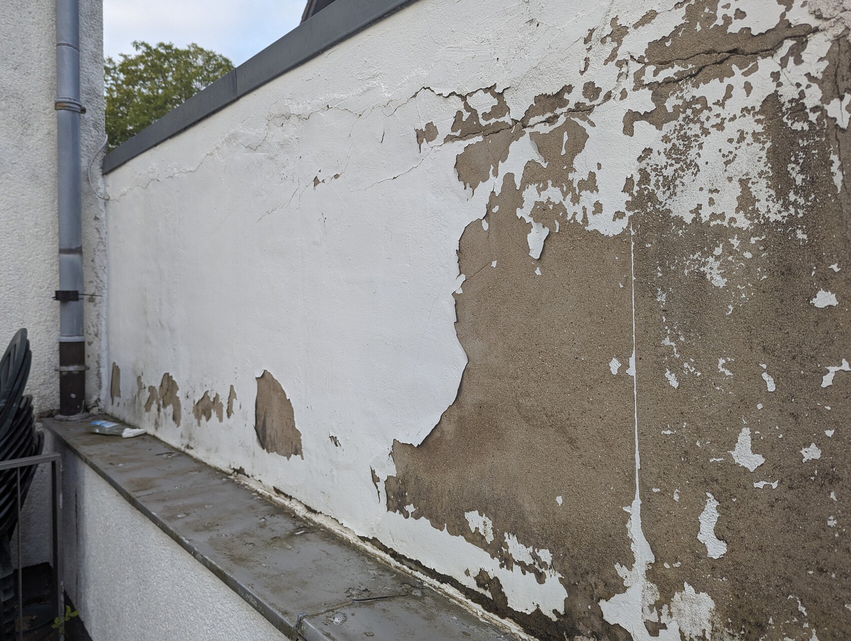 Aussenwand mit abblatternder weissfarbe; brauner Untergrund sichtbar, links Abflussrohr.