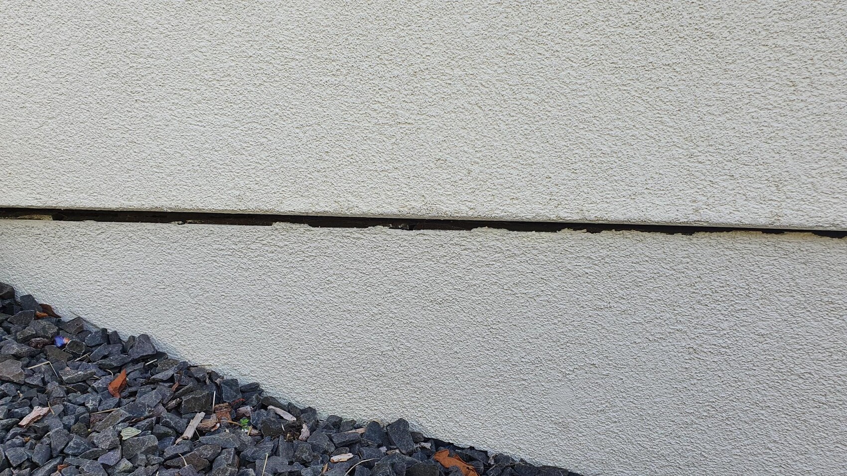 Außenwand aus grobem Putz mit deutlich waagrechter Rissfuge; Kiesel am Boden links.