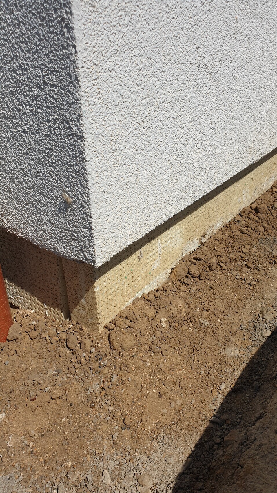 Außenwand mit rauem weißen Putz, darunter beige Fundament am Erdreich.
