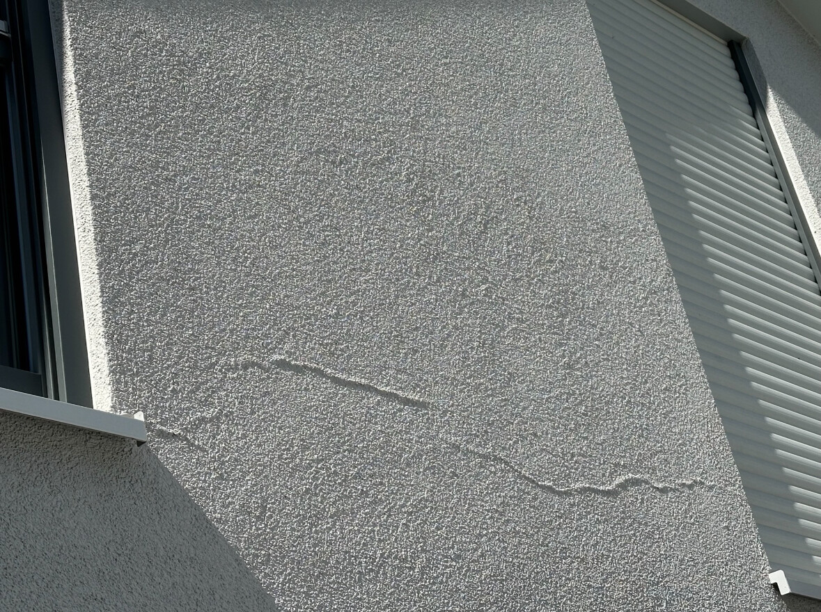 Außenwand mit rauer Putztextur, sichtbare Risslinie; Fenster links, Rollladen rechts.