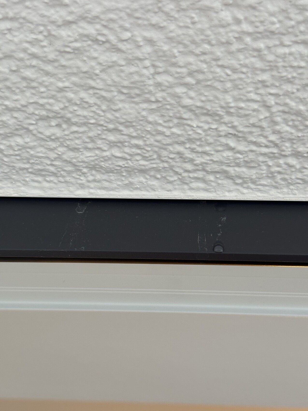 Nahaufnahme einer rauen weißen Außenwand über einer dunklen Leiste, darunter helles Panel.
