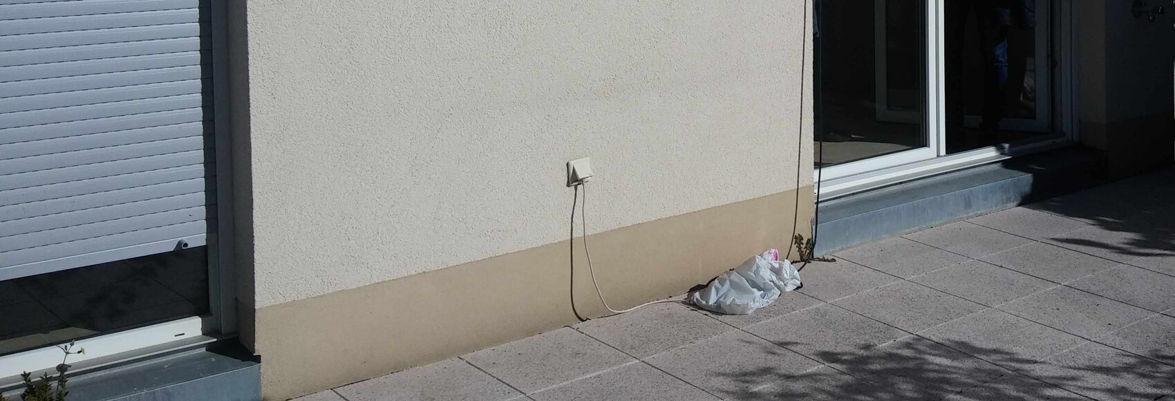 Aussenwand eines Hauses mit Steckdose, Kabeln und Muellbeutel auf Terrasse