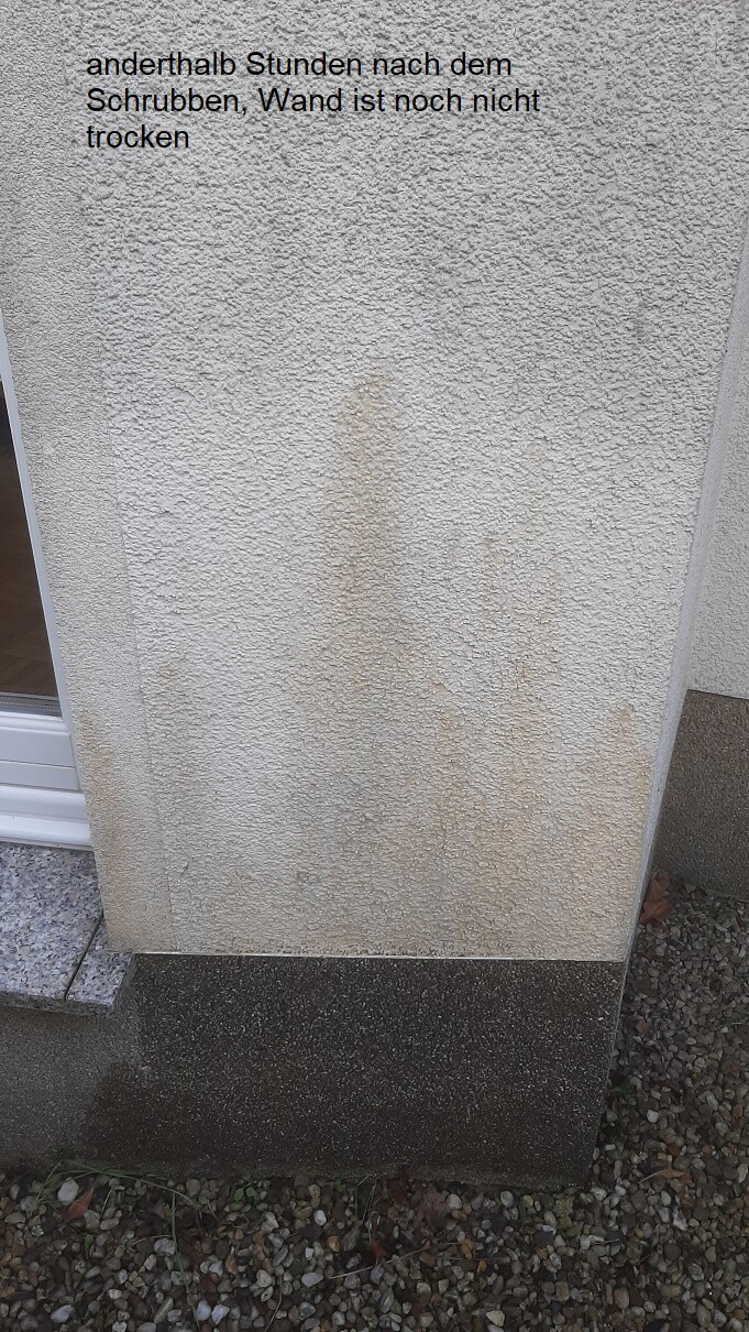 Außenwand mit rauer Putzstruktur und dunklem Fundament neben Tür