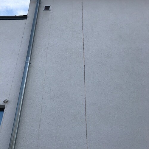 Außenwand mit vertikalem Riss und sichtbar installiertem Fallrohr