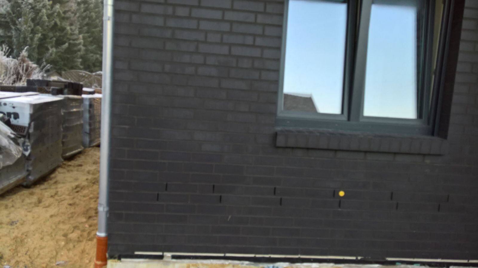 Außenansicht eines Hauses mit dunkler Ziegelwand, Fensterfront und Baucontainer links.