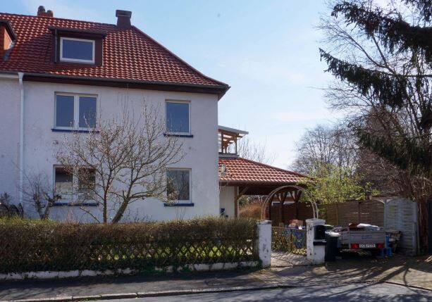 weißes zweistöckiges Wohnhaus mit rotem Ziegeldach, Gartenzaun und Zufahrt.
