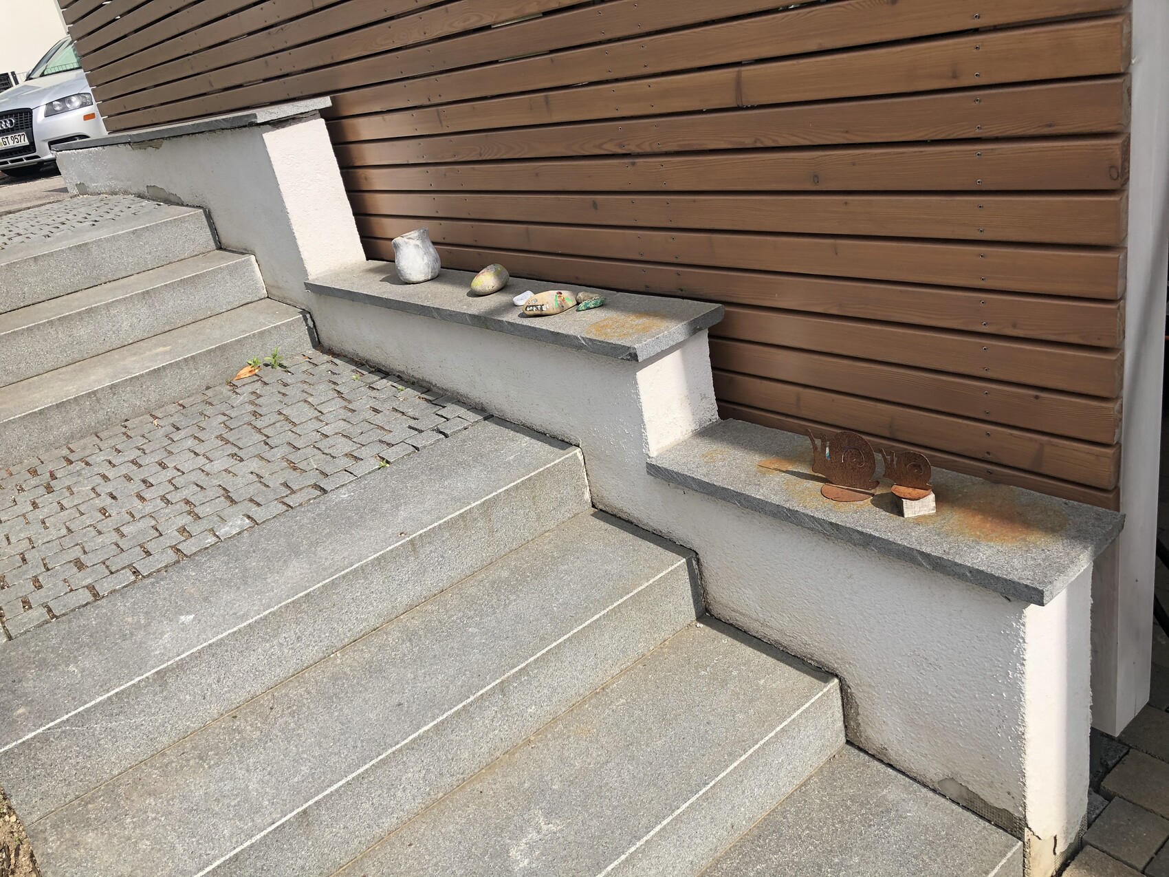 Außenstufen aus Beton, Sitzbank aus Stein mit Steinen und rostigen Metallfiguren; Auto