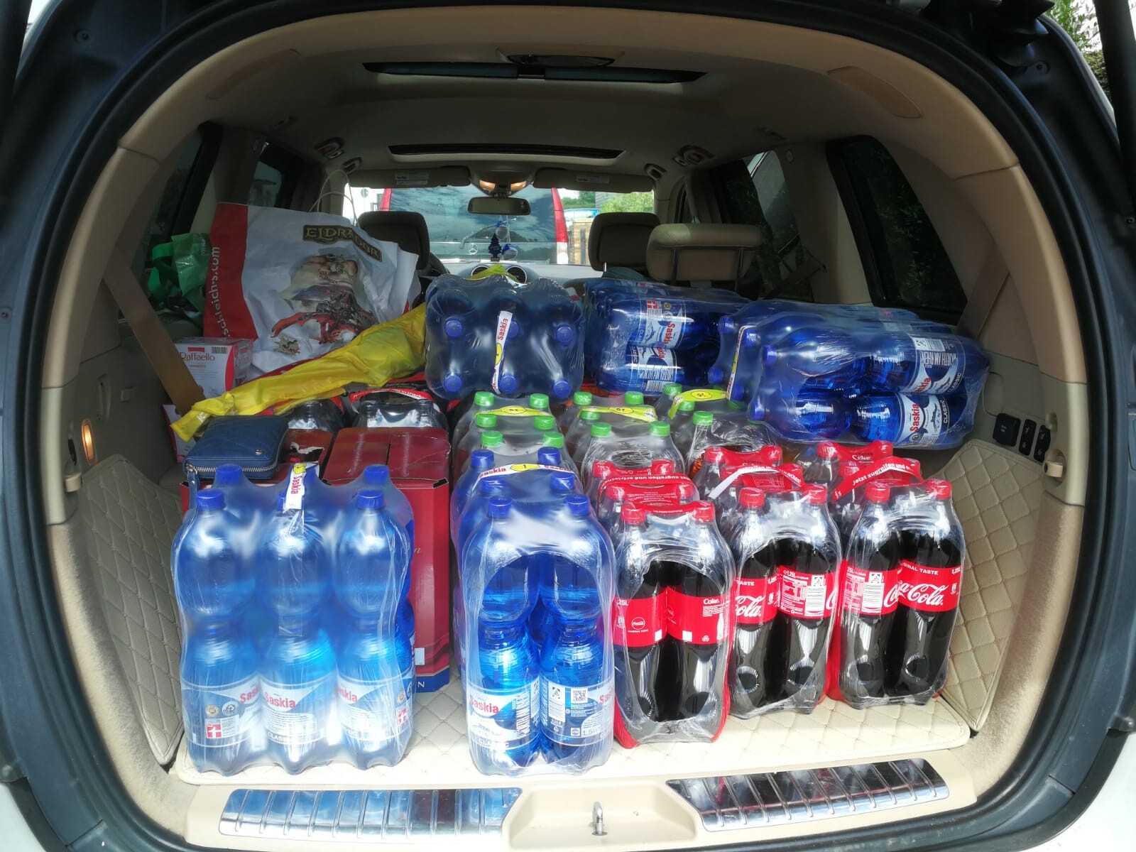 Kofferraum eines Autos voll beladen mit Getränkekästen: Wasserflaschen und Cola-Flaschen.