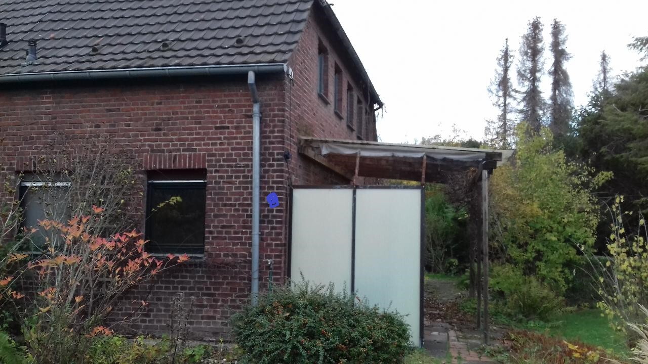 Ziegelhaus mit undurchsichtiger Glas-Trennwand im Garten und verwitterter Pergola.