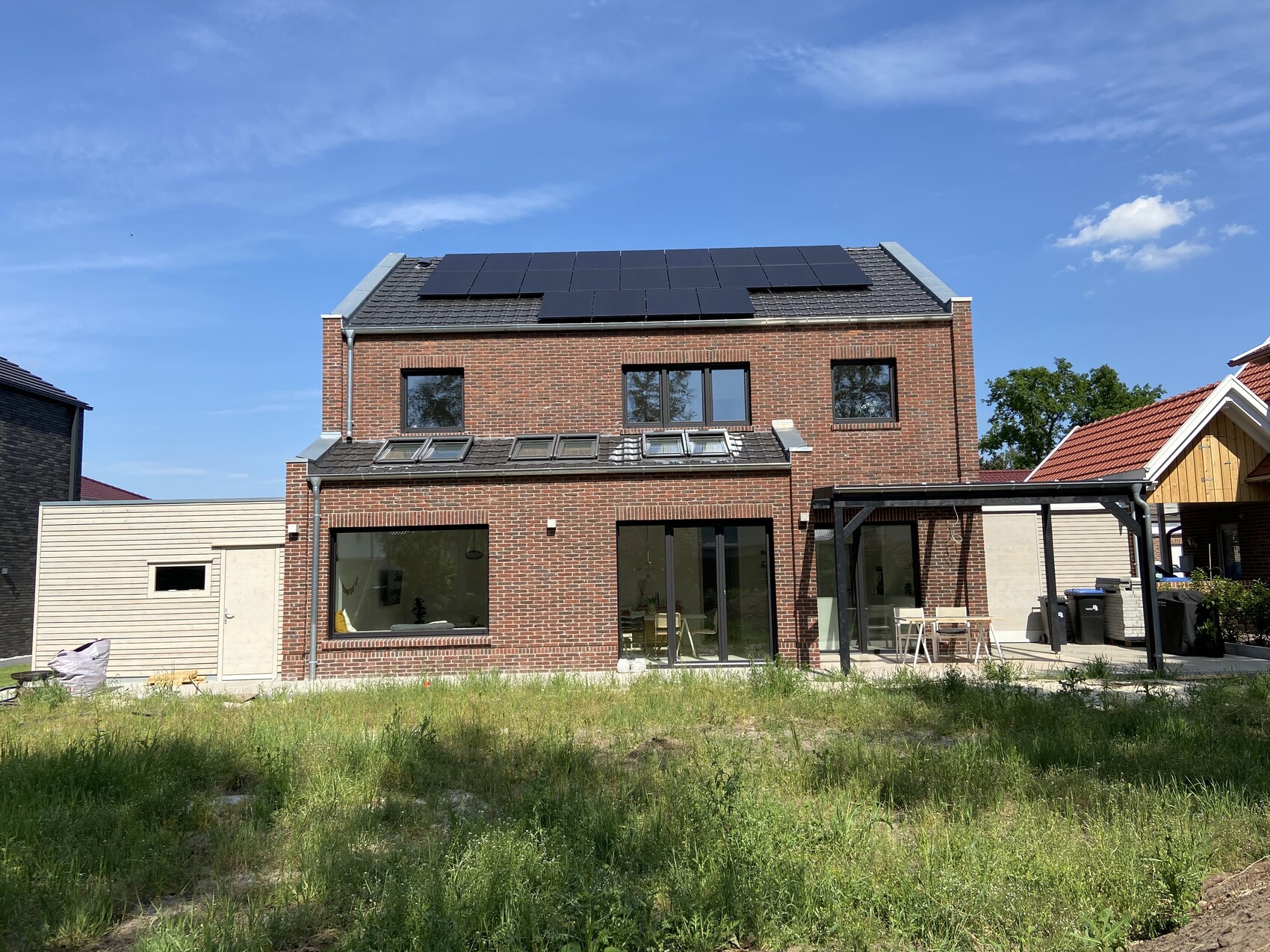 Zweistöckiges Ziegelhaus mit Solarmodulen, Glasfronten und überdachter Terrasse.