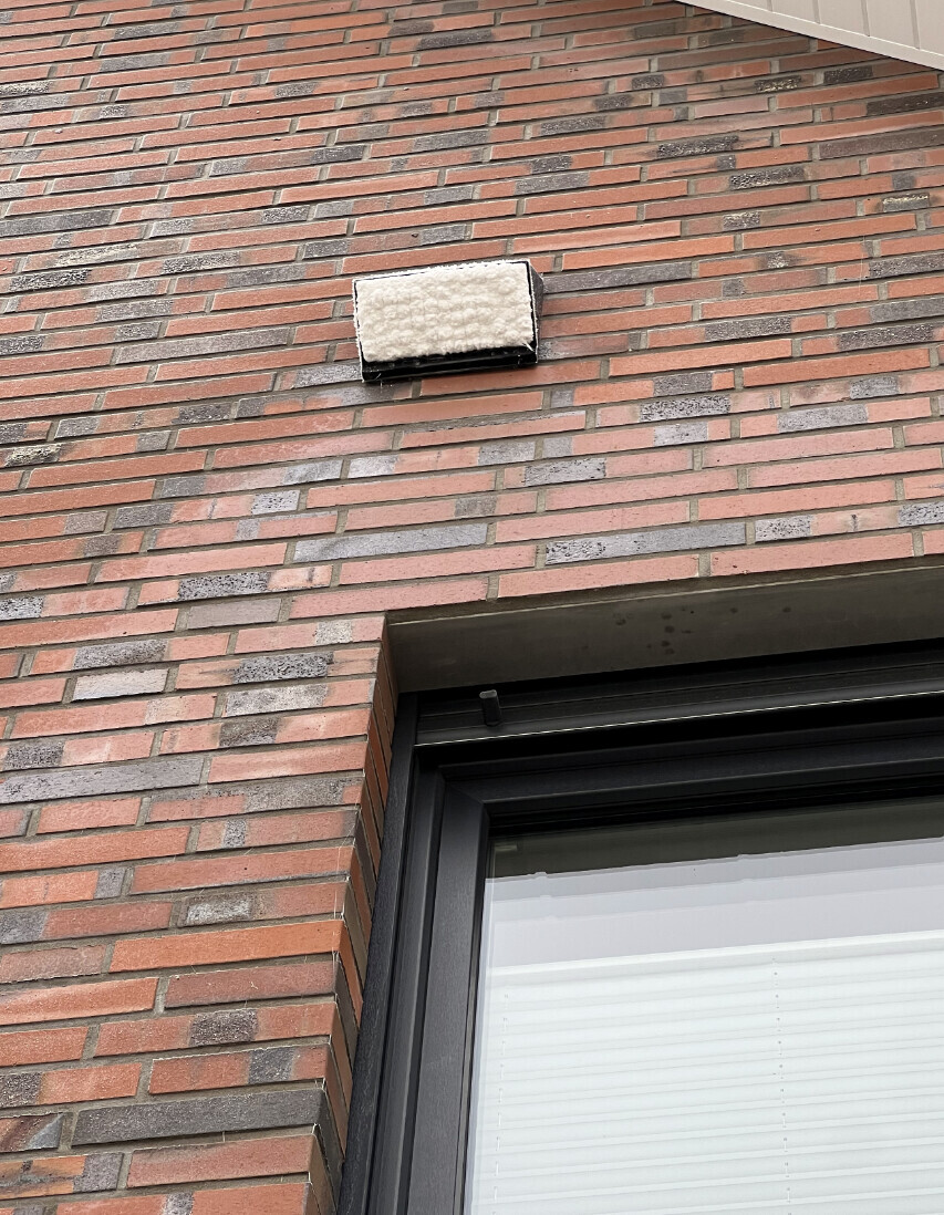 Außenwand aus roten Ziegeln mit einer rechteckigen Außenleuchte, Schnee bedeckt über dem Fenster.