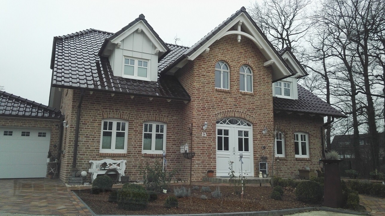 Ziegelhaus mit Backstein, dunklem Ziegeldach, weißen Fenstern, weißem Eingang, Garage links