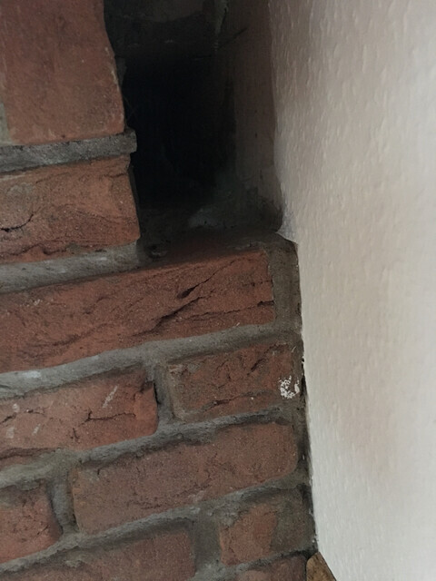 Ecke aus roten Backsteinen mit dunkler Öffnung neben der weißen Wand.