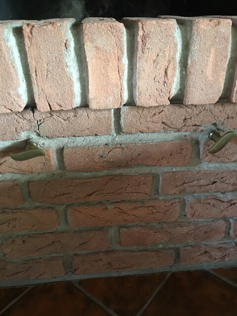 Nahaufnahme einer hellbraunen Backsteinwand mit grauen Fugen und zwei gebogenen Metallgriffen.