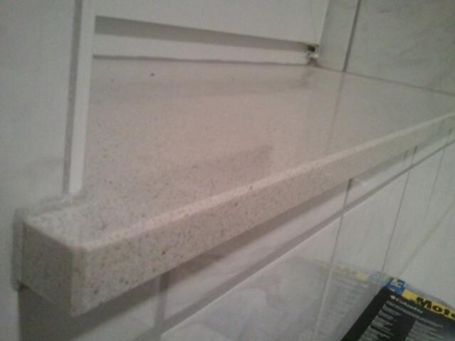 Beige gesprenkelte Badablage aus Stein an Fliesenwand