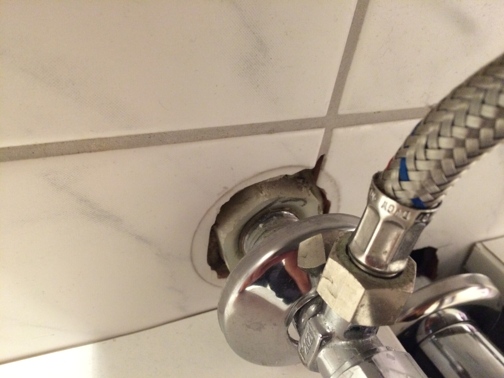 Chromarmatur mit geflochtenem Schlauch; Fliesenwand mit Loch hinter dem Anschluss.