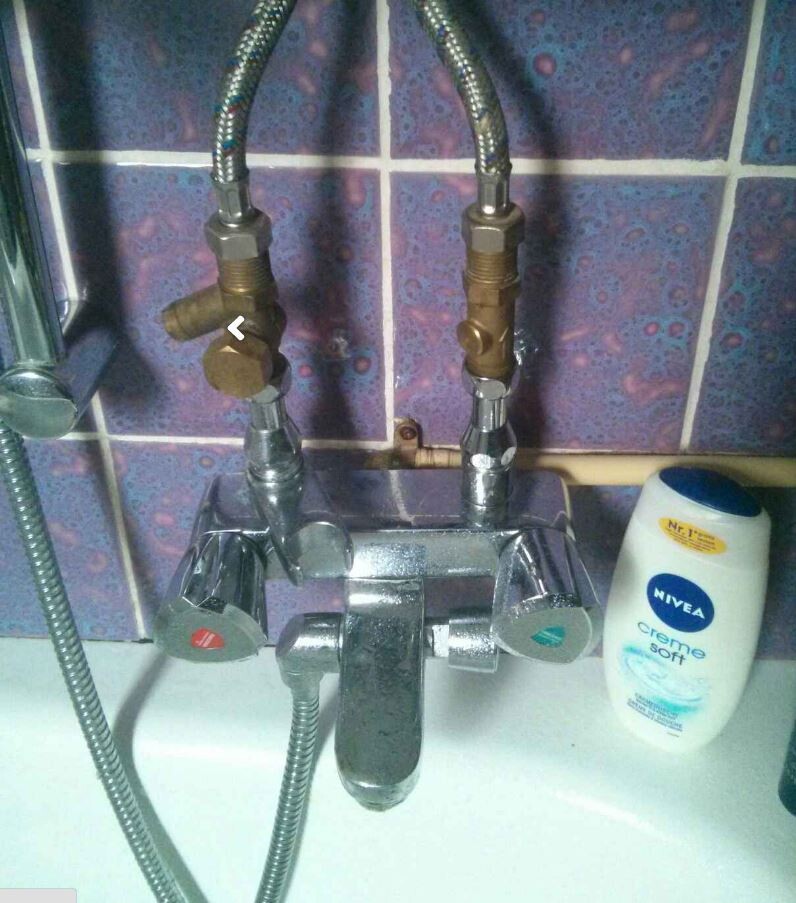 Badezimmer Armaturen mit zwei Griffen und flexiblen Brauseschlauch vor Fliesenwand