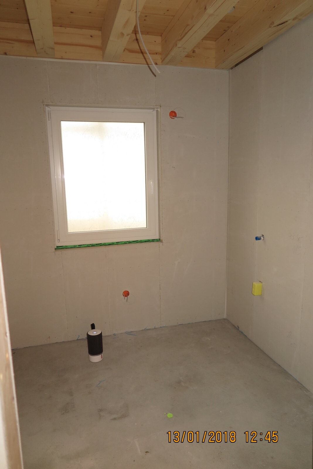 Badezimmer im Rohbau mit sichtbaren Installationen, Fenster und Holzbalkendecke