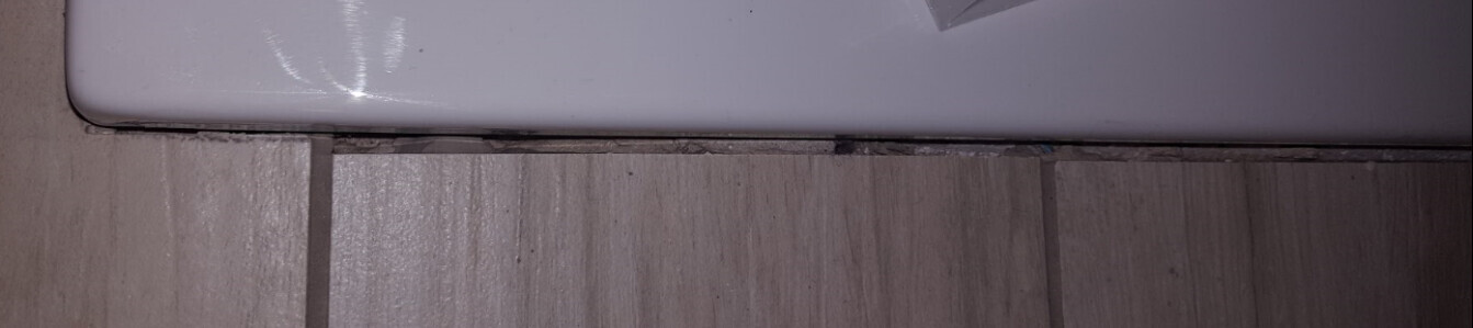 Nahaufnahme der Badewannenkante und Fliesenboden im Badezimmer mit Spalt zwischen Wanne und Boden