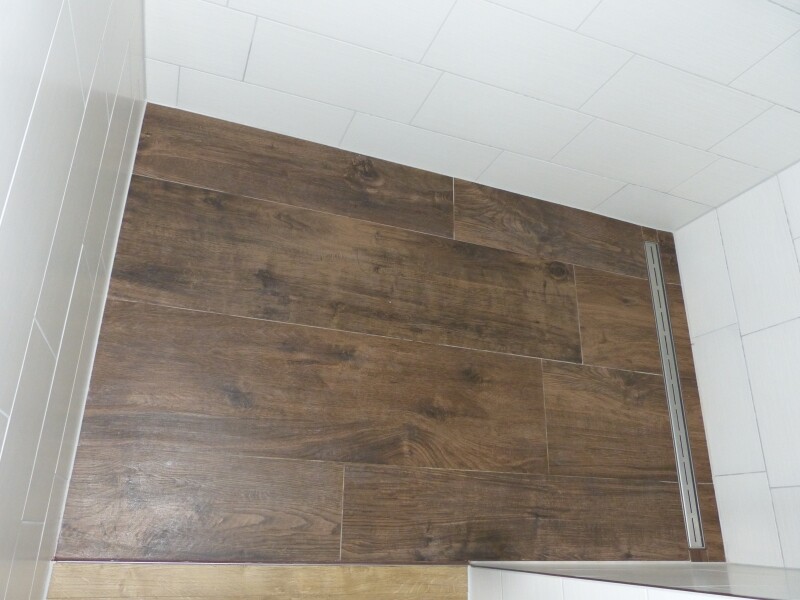 Badezimmerboden in Holzoptikfliesen mit Dusche und weißen Wandfliesen.