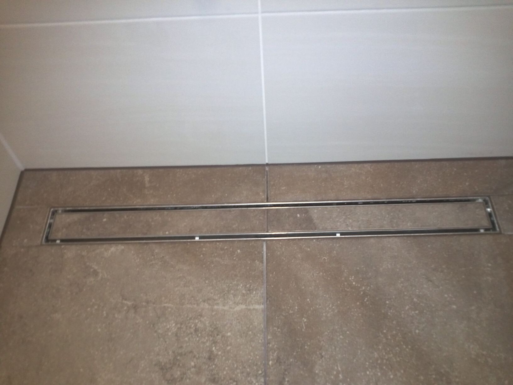 Langer rechteckiger Metallabfluss in braunem Fliesenboden im Badezimmer.
