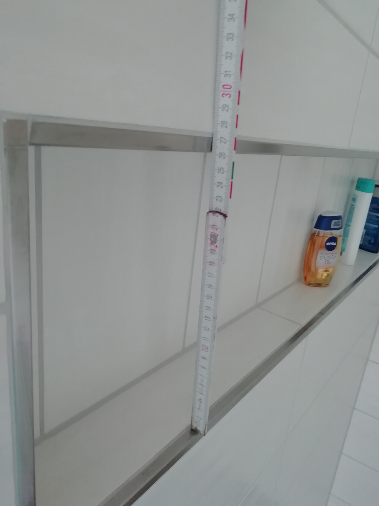 Badezimmer Dusche mit Glaswand, Maßband angelegt, Fliesenwand und Shampoo-Flaschen auf Ablage