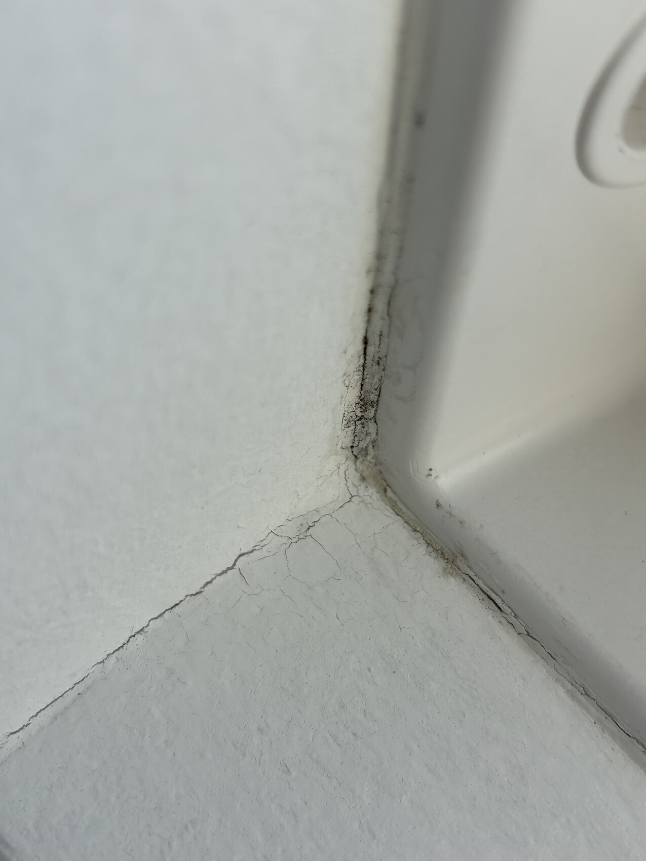 Weiße Badewannen-Ecke mit Rissen in Fugen und beschädigter Dichtmasse.