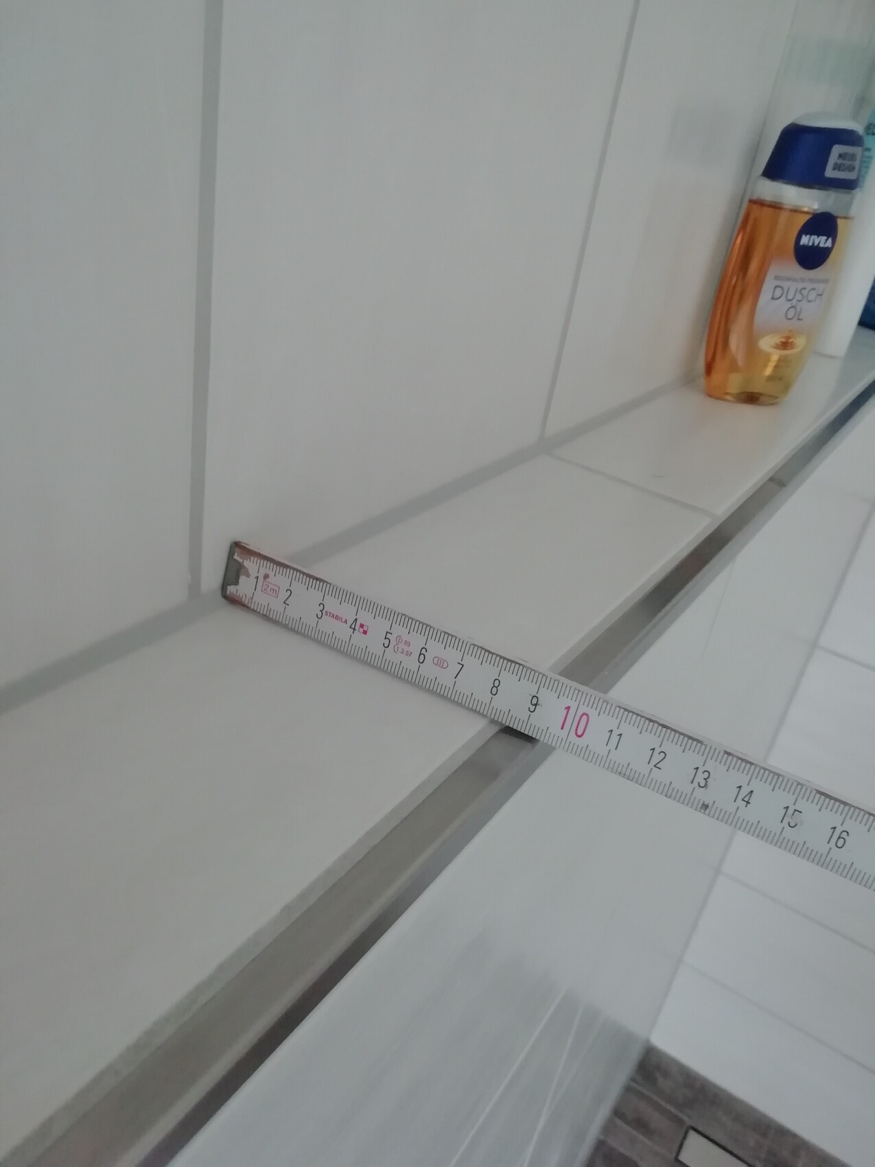 Messband liegt quer auf weißer Badezimmerablage neben Duschöl-Flasche.