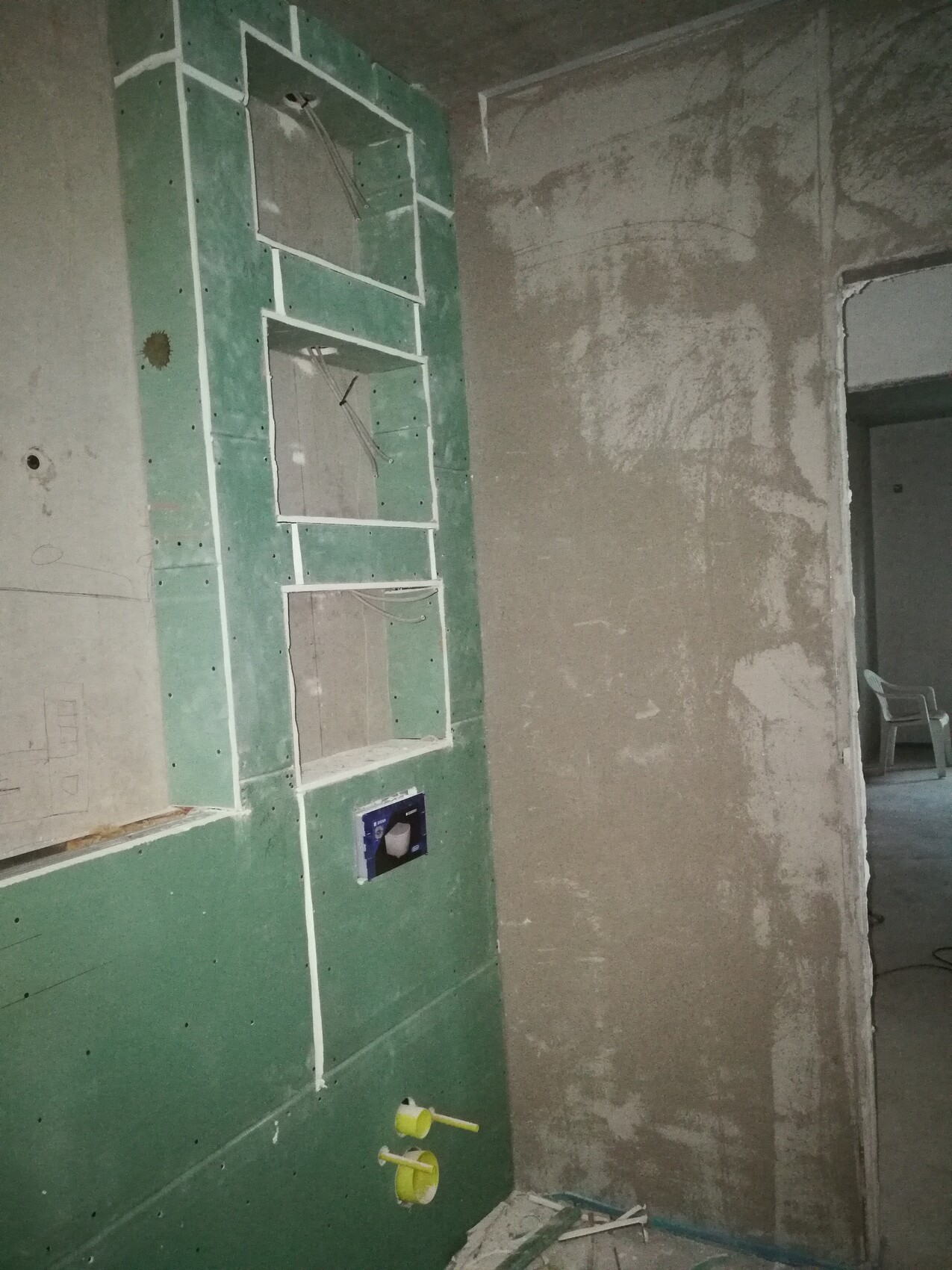 Grüne Trockenbauwand mit Nischen, sichtbare Kabel, offenes Steckdosenloch, Baustelle im Hintergrund
