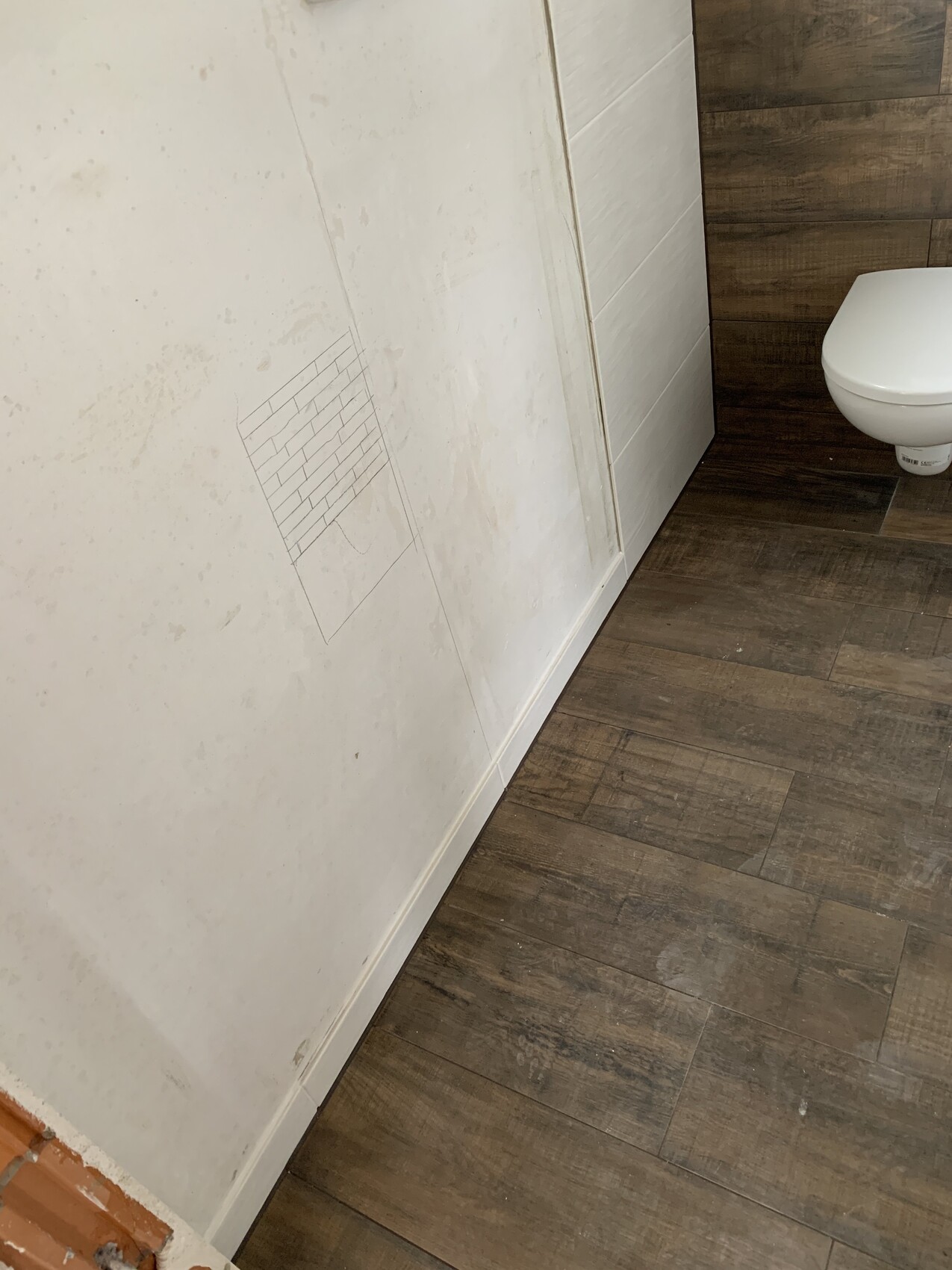 Badezimmer mit dunklem Boden, weißer Wand und gezeichneter Fliesen-Skizze; rechts WC.