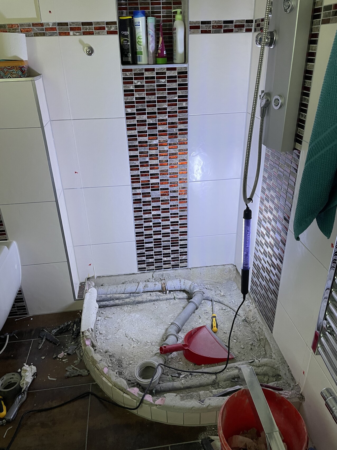 Badezimmer-Renovierung: freiliegende Rohre, Schutt, Putzreste, Eimer und Werkzeuge auf dem Boden.