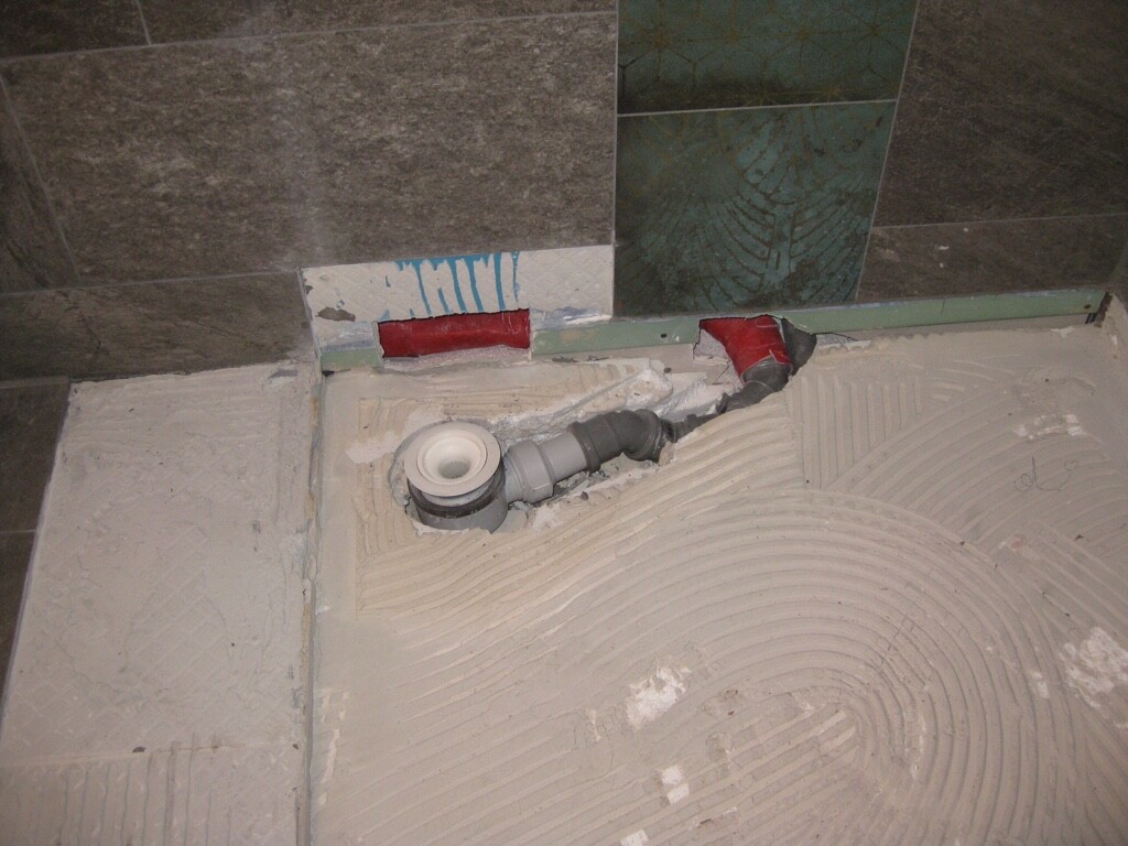 Badezimmerboden mit Fliesen, offene Rohrleitungen sichtbar