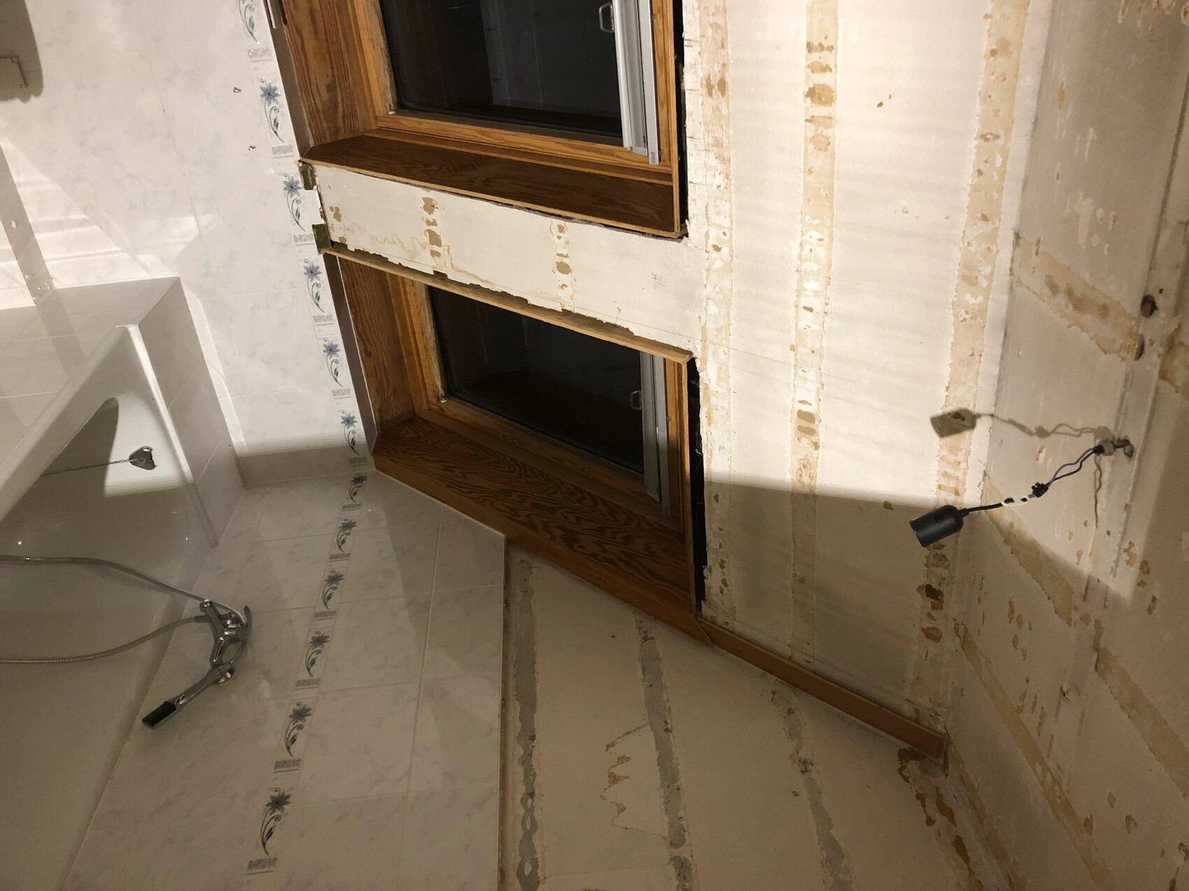 Badezimmer im Umbau mit freigelegten Wänden, Fliesen, Fensterrahmen und offener Elektroinstallation