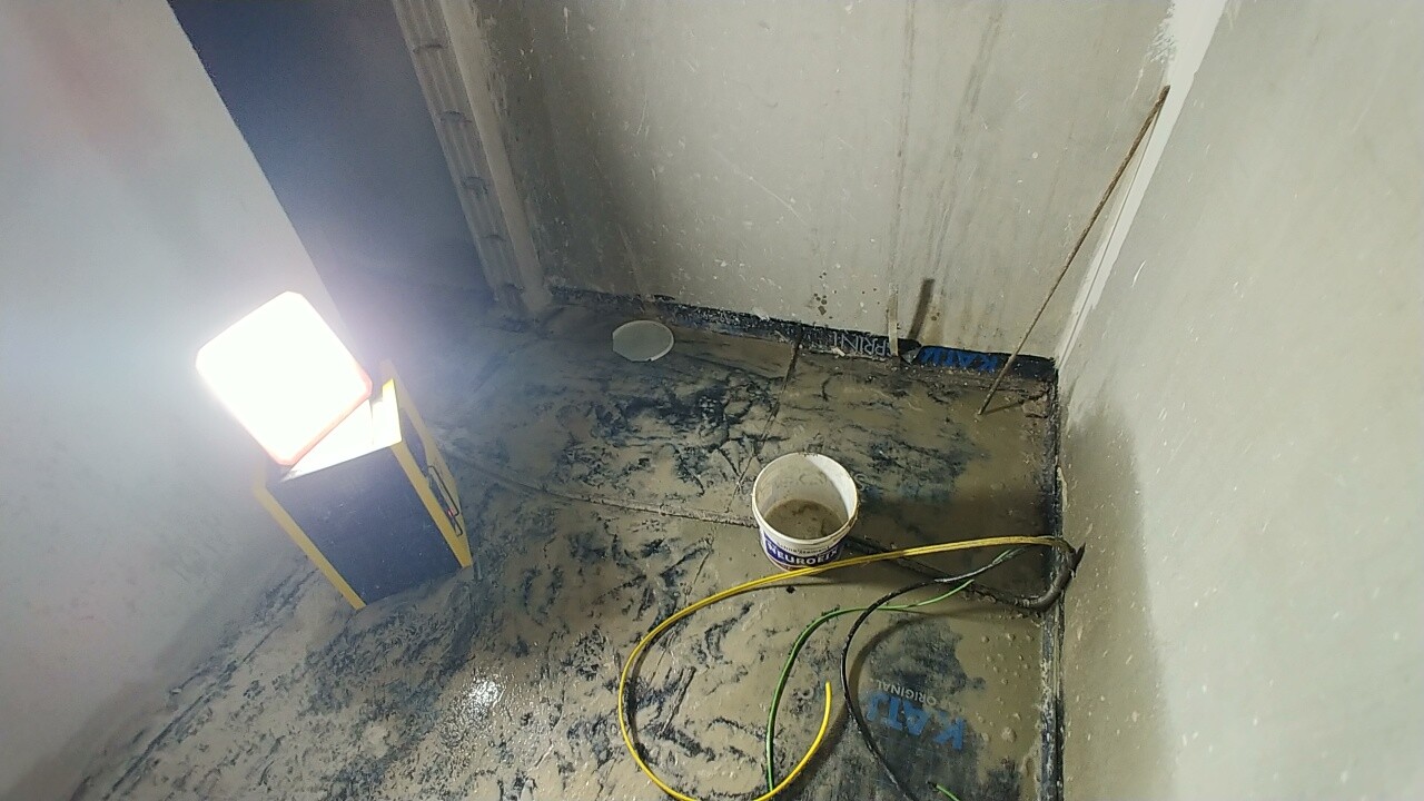 Badezimmer-Baustelle mit Eimer, Kabeln und nassem Boden