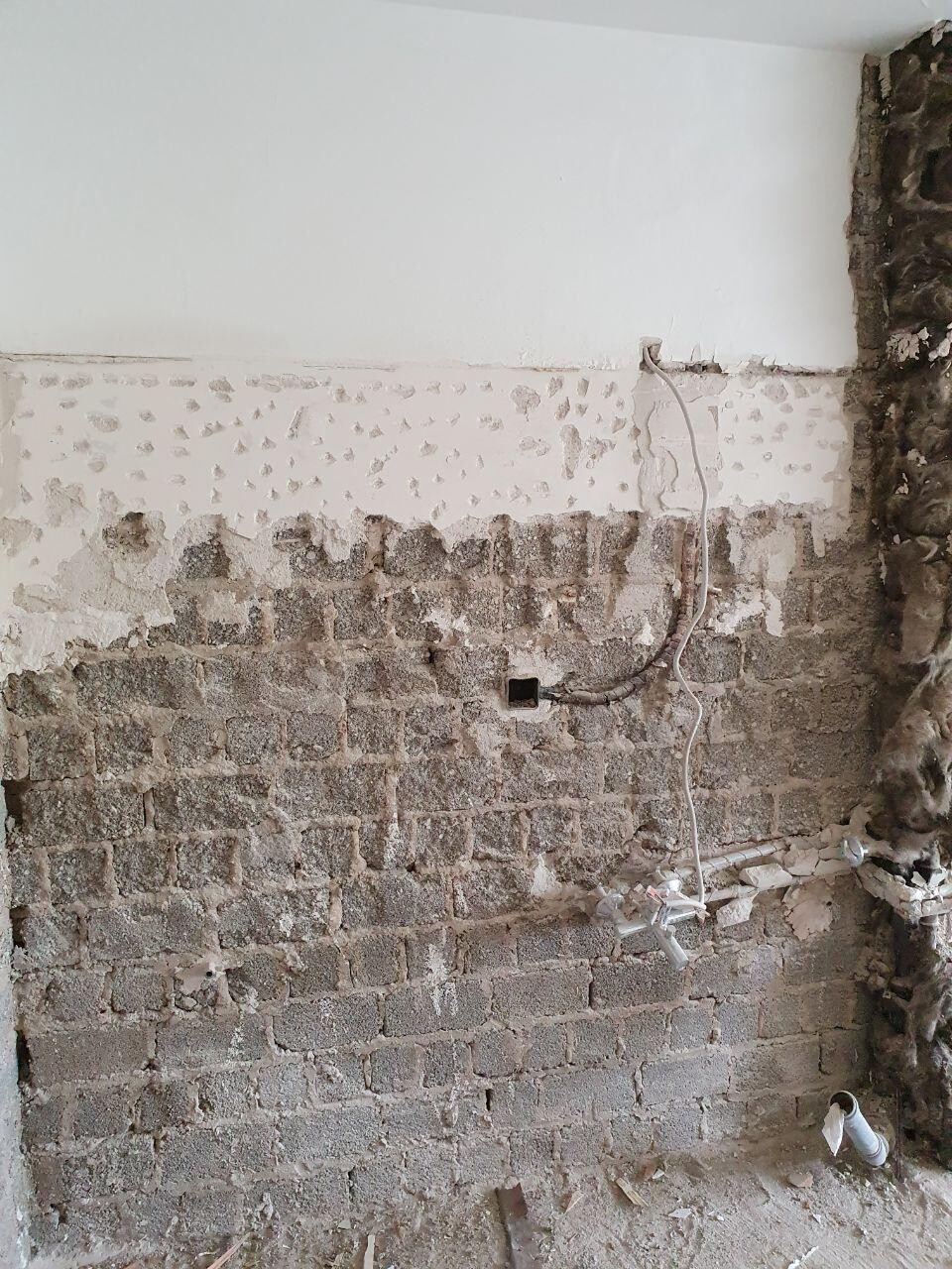 Unverputzte Badezimmerwand mit Ziegeln, Putzresten, Kabeln und Sanitärrohren.