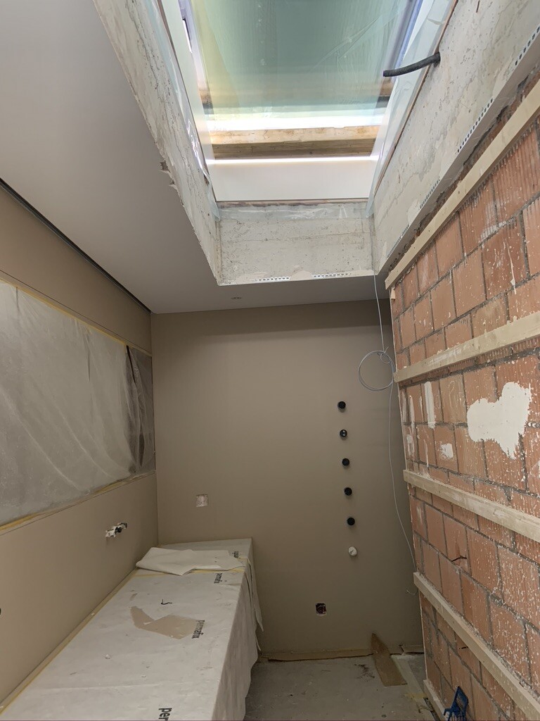 Schmaler Renovierungsraum mit Dachfenster, rechte Ziegelwand und Wandanschlüsse.