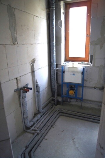 Badezimmerrohbau mit sichtbaren Sanitärrohren, Installationsrahmen und Fenster