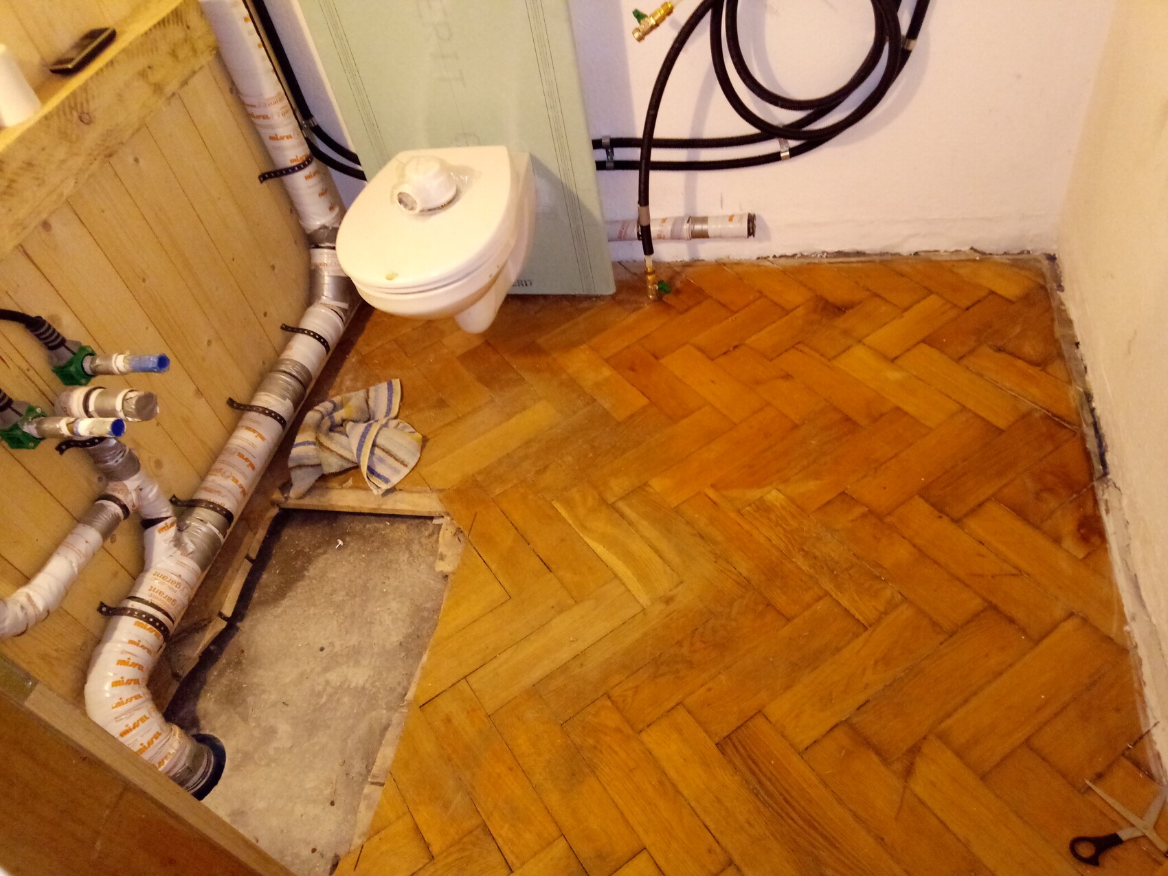 Bad mit sichtbaren Rohren, Sanitärinstallationen und Holzboden unter Renovierung.